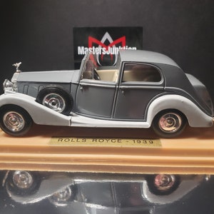 Könnte beinhalten: Ein graues 1939 Rolls Royce Modellauto auf einem Ausstellungsständer. Das Auto hat eine schwarze Innenausstattung und verchromte Räder.