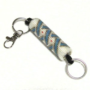 May include: A white beaded keychain with blue and gold accents. The keychain has a silver ring and a silver clip.