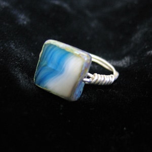 May include: A silver ring with a square blue and white agate stone.