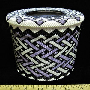 May include: A white, black, and purple beaded tissue box cover with a geometric pattern. The cover is cylindrical and has a round opening on the top.