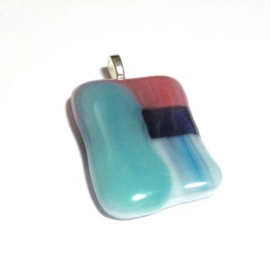 May include: A colorful glass pendant with a silver bail. The pendant features a blend of colors, including teal, red, blue, and white. The abstract design is smooth and rounded, with a glossy finish. A unique piece of wearable art.