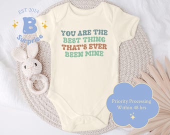 May include: A cream-coloured baby onesie with the text "You are the best thing that's ever been mine" in colourful retro font.