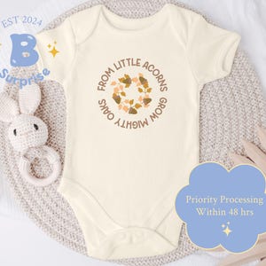 May include: A white baby onesie with a brown and orange acorn design and the text "From Little Acorns Grow Mighty Oaks".