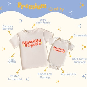 May include: Two cream-coloured t-shirts with the text "Beautified Surprise" printed in red. The larger t-shirt has short sleeves and a crew neck. The smaller t-shirt has short sleeves and a snap closure at the bottom. Both t-shirts are made of 100% cotton interlock.
