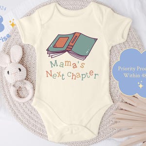 May include: A white baby onesie with short sleeves features a colorful illustration of a book with the text "Mama's Next Chapter".
