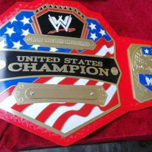 May include: A red, white, and blue wrestling championship belt with the words "United States Champion" on the front. The belt has a gold eagle design on the side plates.