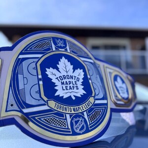 Könnte beinhalten: Ein blauer und goldener Meisterschaftsgürtel mit dem Logo der Toronto Maple Leafs und den Worten "Toronto Maple Leafs" und "NHL".