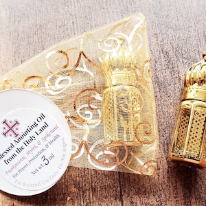 May include: A small glass bottle with a gold-coloured ornate cap and metal lattice overlay, accompanied by a gold organza drawstring pouch and a round white tag labelled Blessed Anointing Oil from the Holy Land, Net wt. 3 ml.
