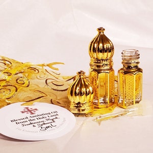 May include: Two small glass bottles with gold-coloured ornate caps, one with the cap removed, alongside a clear glass dropper. A round white tag reads Blessed Anointing Oil from the Holy Land, Frankincense, Myrrh, & Spikenard, 3ml. A gold organza bag.