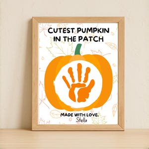 May include: A framed print featuring an orange pumpkin with a handprint in the center. The text reads "Cutest Pumpkin in the Patch" and "Made with Love, Stella". The artwork is set against a white background with fall leaves.