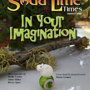 Peut inclure: Une perle en verre blanc avec un motif de souris sur le dessus, posée sur une base en verre vert avec un tourbillon rose. La perle est sur une surface blanche avec une branche de bois et de la mousse en arrière-plan. Le texte "Soda Lime Times" et "In Your Imagination" est visible en arrière-plan.