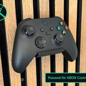 Könnte beinhalten: Ein schwarzer Xbox-Controller, montiert auf einer Holzoberfläche. Der Controller wird von einer schwarzen Halterung gehalten. Das Bild enthält ein grünes Feld mit dem Text "Passend für XBOX Controller".