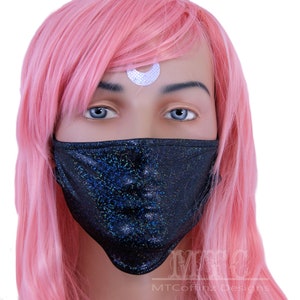Könnte beinhalten: Eine schwarze Gesichtsmaske mit glitzerndem Finish. Die Maske wird von einer Puppe mit pinkfarbenem Haar und einem silbernen Halbmond-Aufkleber auf der Stirn getragen.