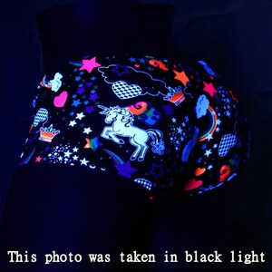 May include: Black shorts with a neon unicorn, stars, hearts, and rainbows design. The shorts are glowing under a black light.