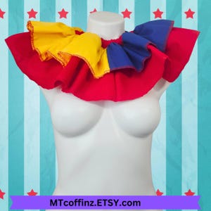 May include: A red, yellow, and blue ruffled collar. The collar is made of fabric and has a layered design. It is a costume accessory.