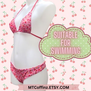 May include: Pink cherry print bikini top and bottom. The bikini top is a triangle style with adjustable straps. The bikini bottom is a high-cut style. The text "Suitable for Swimming" is on a green cloud with white polka dots.