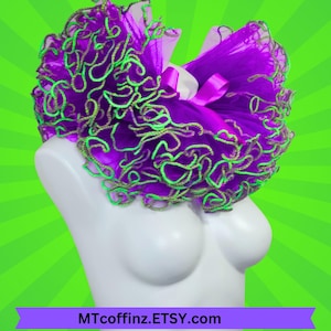 May include: A purple tutu with green and gold trim, displayed on a white mannequin. The tutu has a layered design with a satin ribbon. The background is a bright green with radial lines. The text "MTcoffinz.ETSY.com" is at the bottom.
