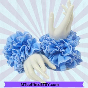 May include: A pair of light blue ruffled wrist cuffs. The cuffs are made of soft fabric and have a delicate, feminine look.
