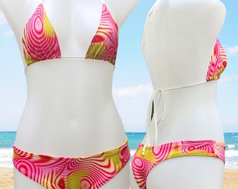 May include: A two-piece bikini set with a vibrant, abstract pattern in shades of pink, yellow, and red. The triangle top and low-rise bottoms are displayed on a white mannequin. The bikini features white string ties. The Etsy shop name is visible.