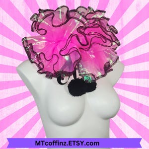 May include: A bright pink ruffled collar with black trim and a black pom-pom accent. The collar is displayed on a white mannequin bust against a pink and white striped background. The text "MTcoffinZ.ETSY.com" is at the bottom.