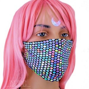May include: A face mask with a holographic iridescent pattern. The mask is made of a stretchy fabric and has a black background. The mask is being worn by a person with pink hair and a crescent moon sticker on their forehead.