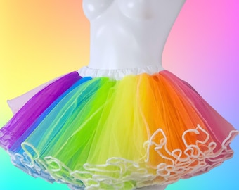 May include: A rainbow-colored tutu skirt with layers of tulle in vibrant hues of purple, blue, green, yellow, orange, and pink. The skirt has a white waistband and a white ruffled trim along the bottom. The Etsy shop name MTcoffinz.ETSY.com is displayed.