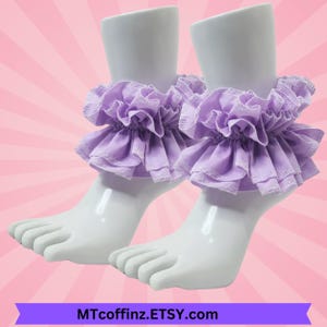 May include: A pair of lavender ruffle ankle cuffs. The cuffs are made of soft fabric and have a delicate, feminine look.