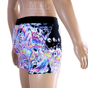 Puede incluir: Pantalones cortos con cintura negra y un vibrante patr&oacute;n arremolinado en tonos de azul, rosa, amarillo y blanco. Los pantalones cortos tienen un panel negro con dise&ntilde;os circulares blancos. El texto "MTCoffinz Designs" es visible.