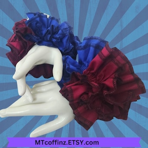 May include: Two ruffled fabric wrist cuffs, one blue and one burgundy, with a white background.