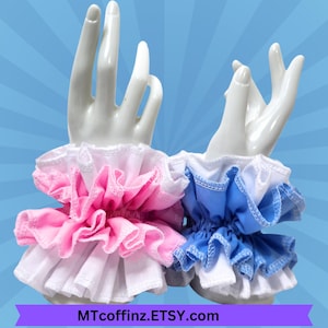 May include: Two ruffled wrist cuffs, one pink and one blue, displayed on white ceramic hands. The cuffs have a layered design with white lace trim. The Etsy shop name MTcoffinz.ETSY.com is displayed at the bottom.