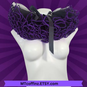 May include: A black and purple ruffled collar with a black satin ribbon. The collar is made of tulle and lace.
