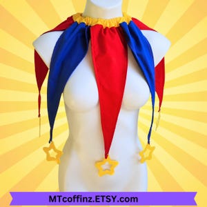 May include: A jester collar featuring alternating red and blue triangular fabric points attached to a yellow gathered neckline. Each point terminates in a yellow star-shaped charm. The text MTcoffinz.ETSY.com is printed on a purple banner below.