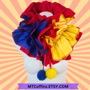 May include: A red, blue, and yellow ruffled collar with two pom-poms attached. The pom-poms are blue and yellow. The collar is made of fabric and has a ruffled design.  MTCoffinz.ETSY.COM