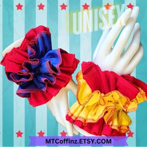 May include: Two pairs of red, yellow, and blue ruffled fabric wrist cuffs. The cuffs are made of three layers of fabric with a red outer layer, a yellow or blue middle layer, and a red inner layer. The cuffs are trimmed with a red or yellow zig-zag stitch.