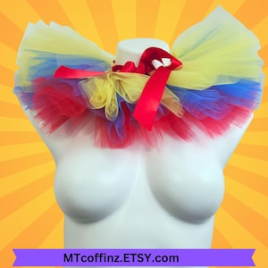 May include: A colorful tutu collar in red, yellow, and blue tulle, accented with a red satin ribbon bow. The collar is displayed on a white mannequin, perfect for costume or cosplay. The Etsy shop name MTcoffinz.ETSY.com is visible.