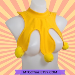 May include: A vibrant yellow top with a high neck and distinctive cut-out pattern. The garment has three fluffy yellow pom-poms and is shown on a mannequin. The Etsy shop name, MTCOFFINZ.ETSY.COM, is displayed at the bottom.