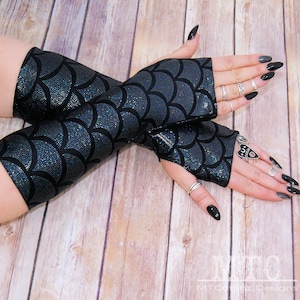 May include: A pair of black fingerless gloves with a silver iridescent mermaid scale pattern. The gloves are made of a stretchy fabric and have a fitted design.