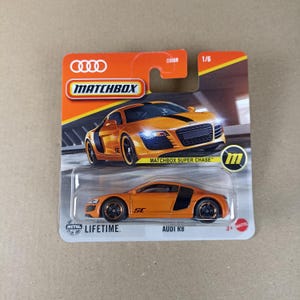 May include: Orange Matchbox Super Chase die-cast toy car of an Audi R8 with black accents and a metal body. The car is on a white card with the Matchbox logo and the words "Matchbox Super Chase" and "Audi R8".