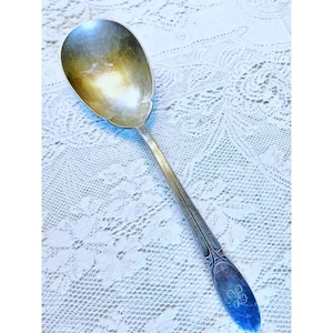 Peut inclure: Une cuillère de service en argent avec un motif orné sur le manche. La cuillère a un monogramme au dos du manche.