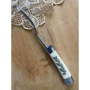 May include: An antique silver and ivory-handled fork with a decorative leaf design. The fork has a curved, slender tine and a rectangular silver ferrule. The ivory handle features a silver leaf pattern. The fork rests on a wooden surface.