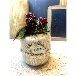 Puede incluir: Un carrete de hilo blanco con un recorte de nota musical en forma de pájaro y un racimo de bayas rojas en la parte superior.