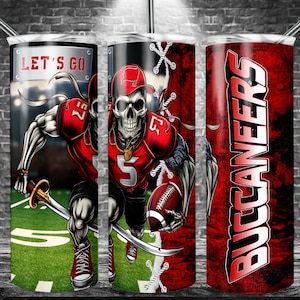 Puede incluir: Un vaso rojo y negro con una calavera que lleva una camiseta de fútbol y sostiene un balón de fútbol. El vaso tiene las palabras "Let's Go" y "Buccaneers".