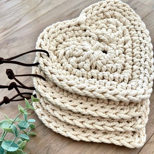 May include: Set of four crocheted heart-shaped coasters in a cream color with brown leather straps.