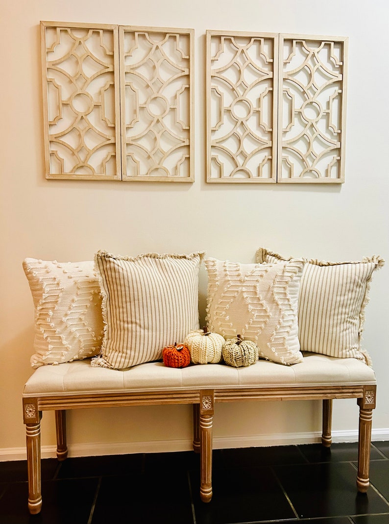 Peut inclure: Un banc blanc avec un coussin beige et quatre coussins. Les coussins ont une bordure en frange et un motif ray&eacute; blanc et beige. Trois petites citrouilles tricot&eacute;es sont sur le banc devant les coussins.