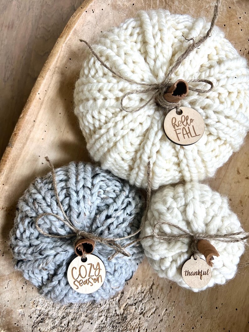 Peut inclure: Trois citrouilles tricot&eacute;es avec des &eacute;tiquettes en bois. Les &eacute;tiquettes disent "hello fall", "cozy season" et "thankful".