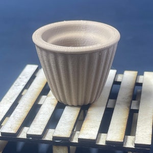 May include: A small, brown, ribbed terracotta pot, sitting on a wooden pallet.