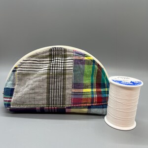 May include: A half-circle patchwork fabric cosmetic bag with a white zipper and a spool of white thread.