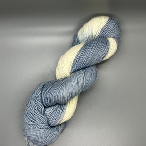 May include: A skein of yarn with a gradient of light blue and white colors. The yarn is twisted into a figure eight shape.