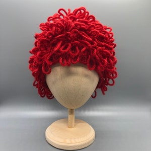 May include: A red yarn wig on a mannequin head. The wig is styled in a curly, messy look.