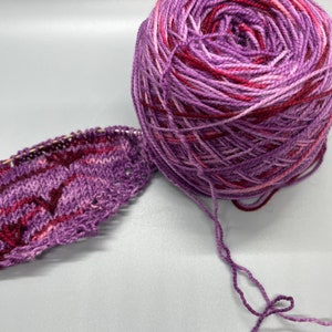 May include: A ball of purple and red yarn with a knitted swatch of the same yarn.